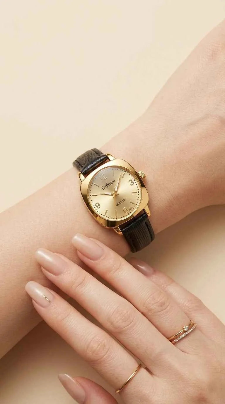 A close-up of a woman's wrist and hand wearing a vintage-style watch with a gold-toned case, gold dial, and dark brown leather strap, set against a soft beige background.