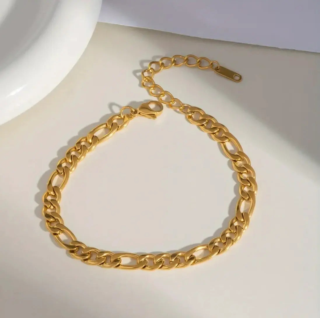 A gold-toned chunky curb chain bracelet with a lobster clasp, arranged in a circle on a light beige surface.