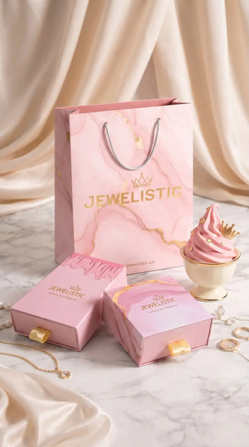 Pink 'Jewelistic' jewelry box, necklace, and cupcake on a marble surface with draped fabric background