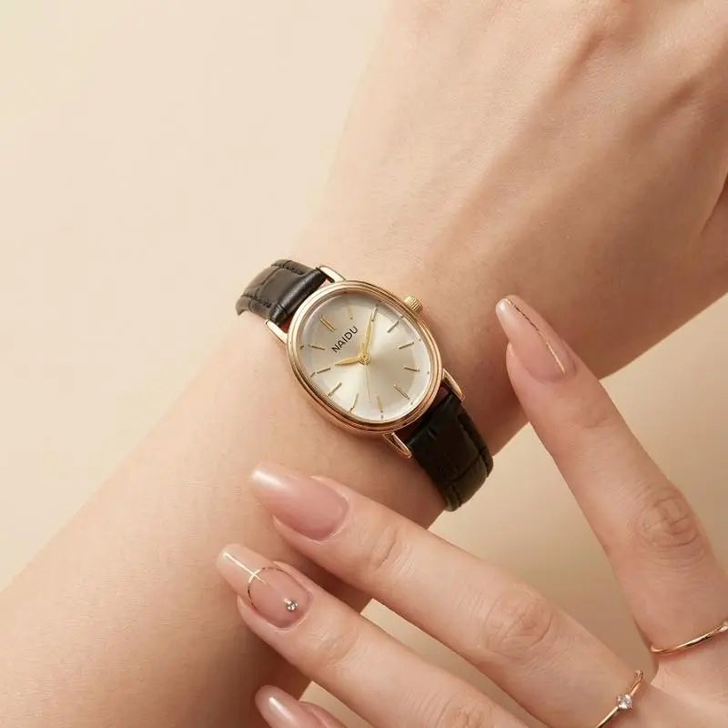 A close-up of a hand holding a NAIDU women's wristwatch with a black crocodile-embossed strap and a gold-tone round dial with a white face.