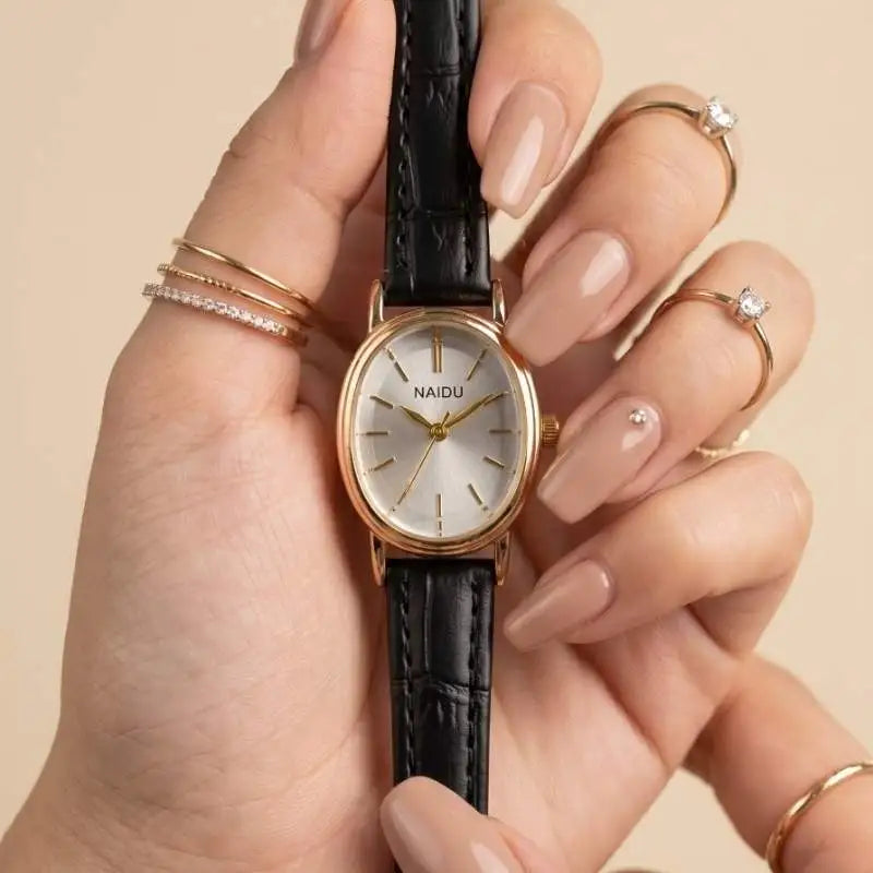 A close-up of a hand holding a NAIDU women's wristwatch with a black crocodile-embossed strap and a gold-tone round dial with a white face.