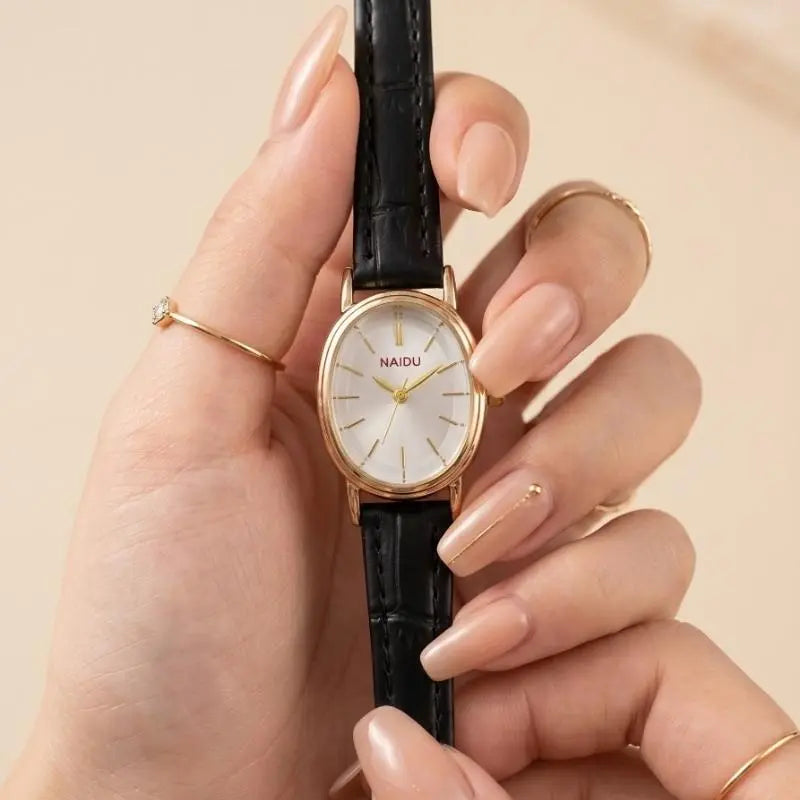 A close-up of a hand holding a wristwatch with a black crocodile-embossed strap, a gold-tone case, and a white dial with gold hands and markers. The brand name 'NAIDU' is visible on the dial.