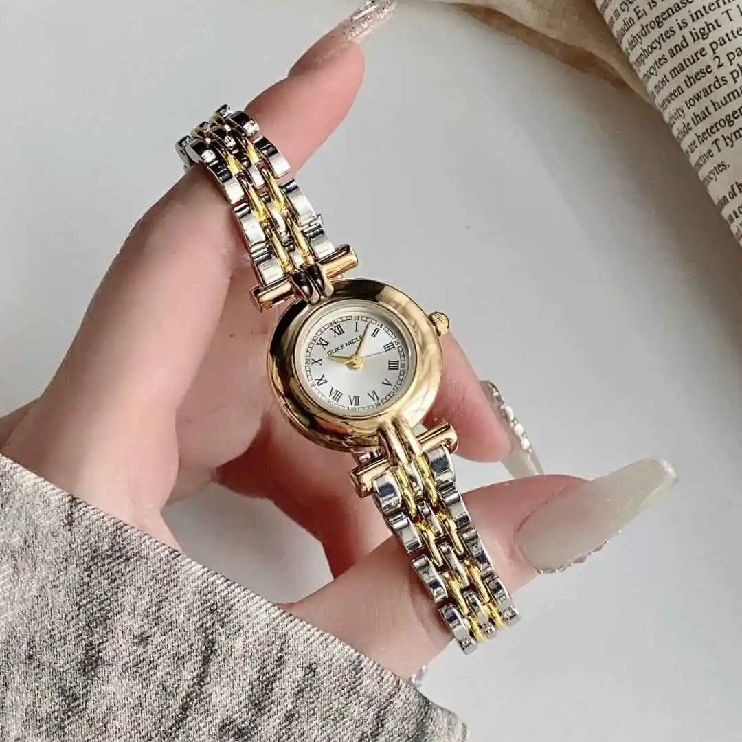 Gold and silver watch held by a hand with a neutral background