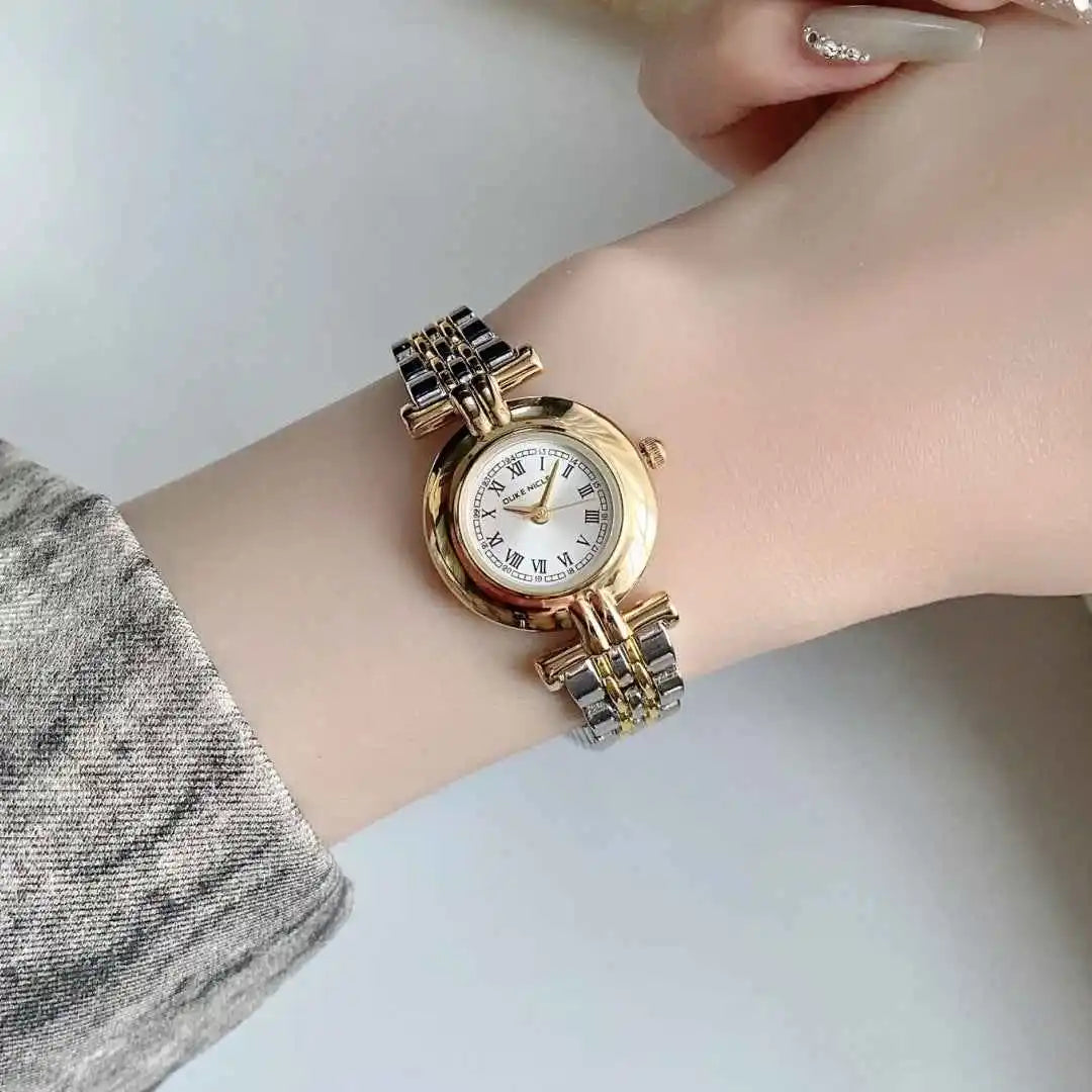 Gold and silver watch on a wrist with a plain background