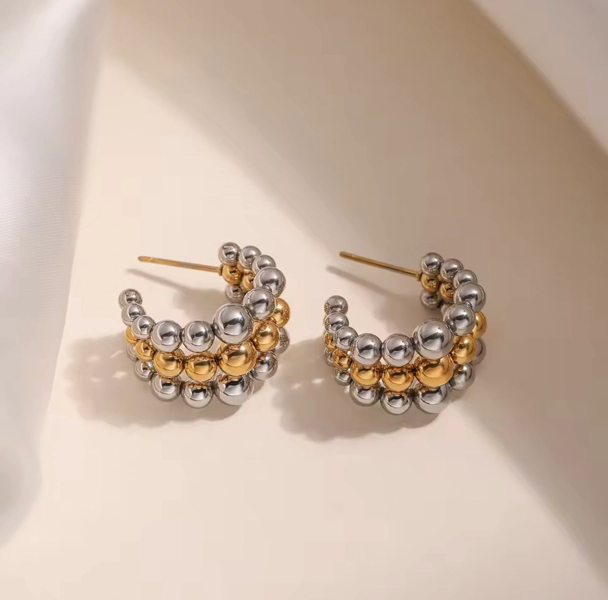 Pair of gold and silver beaded hoop earrings on a light background