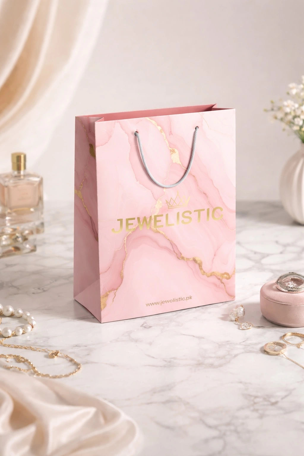 Pink 'Jewelistic' gift bag on a marble surface with jewelry items.