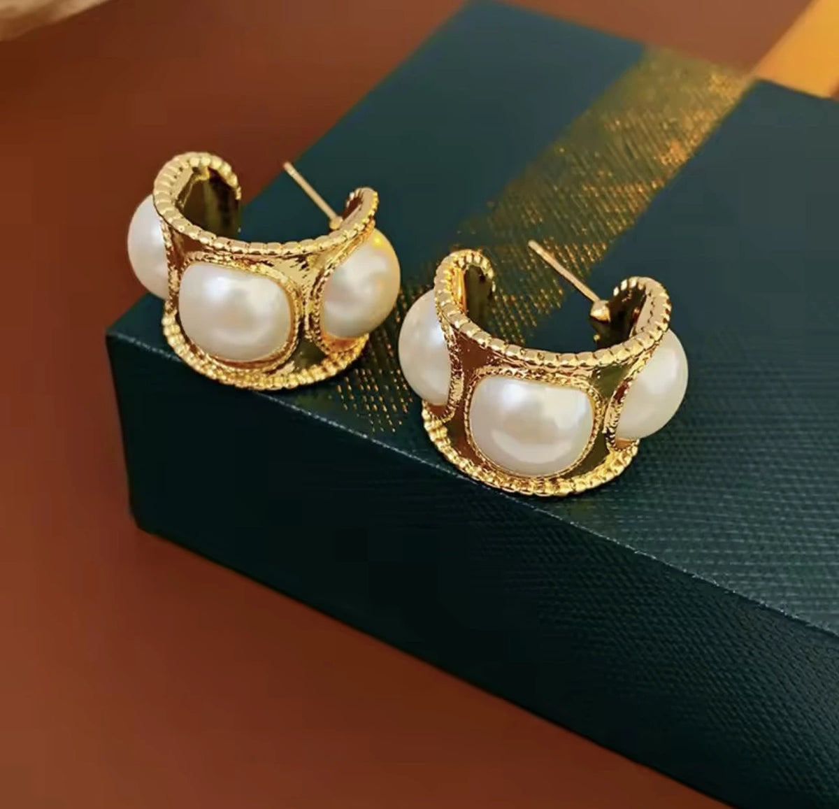 Gold hoop earrings with pearl-like stones on a textured surface